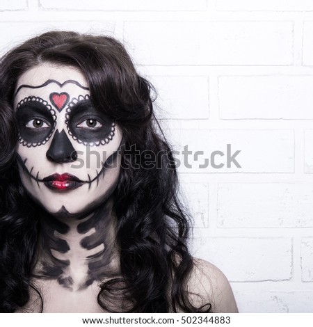 Halloween concept - woman with creative skull make up standing over white brick wall