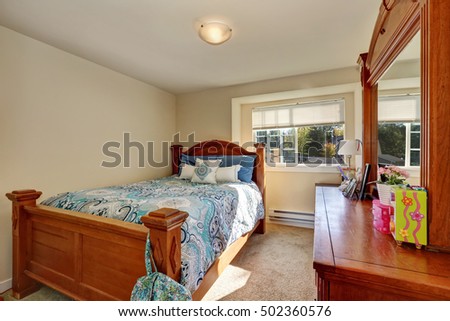 Nice wooden carved bed with colorful bedding and  vanity cabinet in small bedroom. Northwest, USA