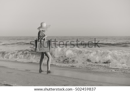 Back side view of woman in summer hat and beach bag standing on the sunny ocean tropic outdoors background