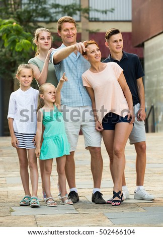 Glad man and woman with four kids walking and pointing aside in town on summer day