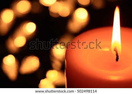 A burning candle with lights in the background.