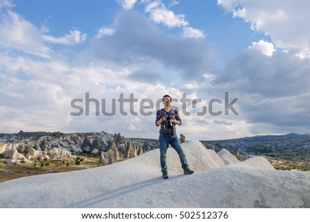 young man taking photo of landscape, standing on rocks in Goreme National Park, typical terrain landscape in Cappadocia, Turkey 
