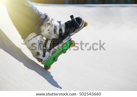 Feet of roller skater wearing aggressive inline skates sitting on a concrete ramp in outdoor skate park. Extreme sports athlete wearing in-line roller skates for tricks and grinds
