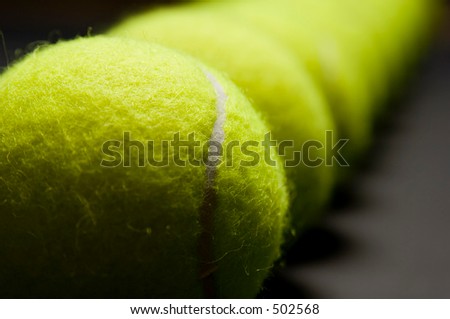 An extreme close-up photograph of a line of tennis balls. Picture has a very shallow depth of fiels with the first ball in line crisply in focus.