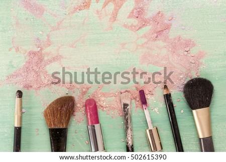 Makeup brushes and lipstick on teal blue background, with traces of powder and blush, forming a frame. Horizontal template for makeup artist's business card or flyer design, with copyspace