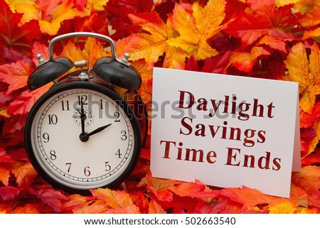 Daylight Savings Time Ends, Some fall leaves, black and white alarm clock and a blank greeting card with copy-space Royalty-Free Stock Photo #502663540