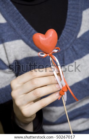 She holds a red heart with a wooden stick. Declaration of love. Decoration