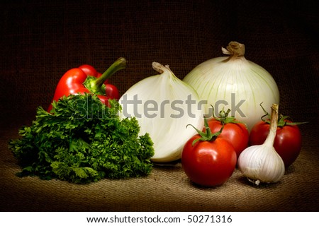 Vegetable country-style still life with tomatoes, onion, bell pepper, parsley and garlic on burlap background