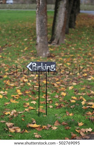 Chalkboard parking sign in a field with autumn leaves and trees.