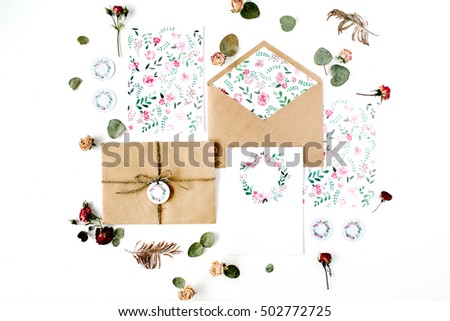 Flat lay workspace. Wedding invitation cards, craft envelopes, pink and red roses and green leaves on white background. Overhead view, top view