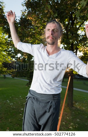 Man walking barefoot on slackline in park with arms out and deep concentrated facial expression.