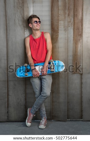 Attractive skater leaning against metal shutters and holding his board