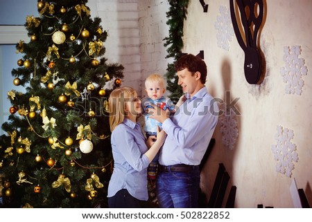 Happy mother and father holding baby son at christmas tree background. Concept of happy family at New Year eve.