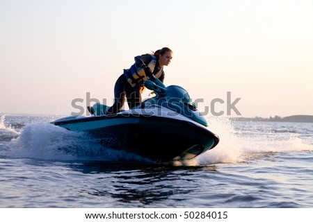beautiful girl riding her jet skis in the sea at sunset. spray