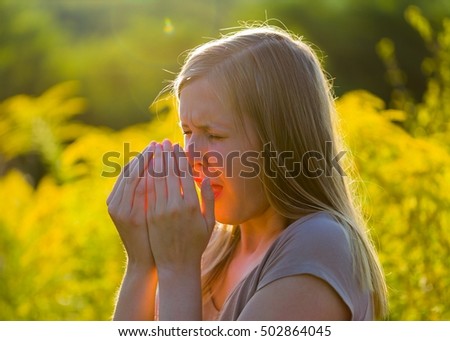 Attractive young woman sneezing because of asthmatic allergy in summer nature.