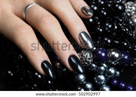 Beautiful female hands with nail polish black and silver color with black and silver beads on a black background
