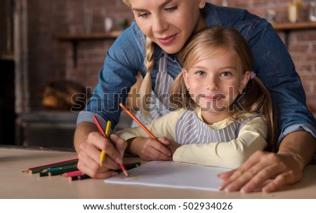 Nice little girl drawing with her mother in the kitchen