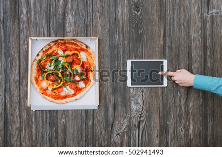 Delicious pizza in a box and woman using an app on a digital tablet, top view