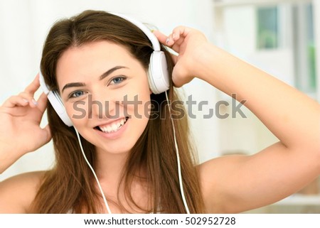 Woman listening music in headphones sitting on sofa in room