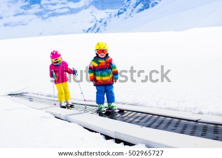 Children on magic carpet ski lift going uphill in the mountains on snowy winter day. Kids in winter sport school in alpine resort. Family fun in the snow. Little skier exercising on a slope.