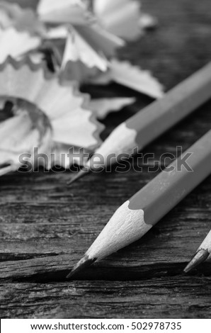 A black and white image of sharpened pencils on a wooden table top.