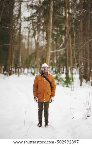 A bearded man with glasses walks through the white snow-covered forest in winter frosty day.