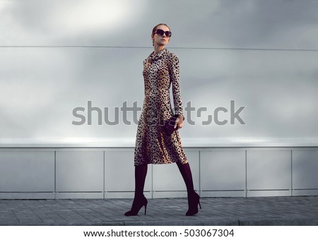 Elegant woman model in leopard dress walking in evening city in shadow, street fashion concept