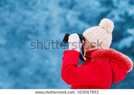 Woman in winter, female photographer takes picture on digital camera outdoors on blurred snowy forest background, blank copy space for advertising text
