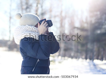 Child little boy photographer takes picture on the digital camera outdoors in winter sunny day over blurred forest background, view profile