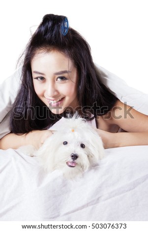 Attractive woman smiling and looking at the camera while lying under a blanket with her dog, isolated white background
