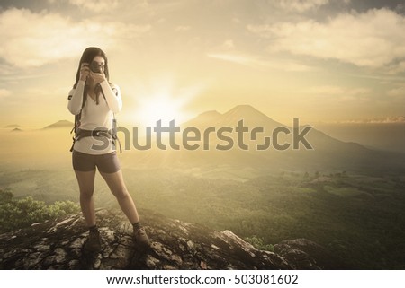 Young woman standing on the rock while taking pictures and looking at the camera