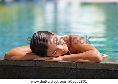 Woman relaxing sunbathing in infinity swimming pool at health spa retreat. Luxurious body care pampering Serene Asian young lady enjoying sun time at resort hotel facilities. Tranquility and comfort. Royalty-Free Stock Photo #503082931