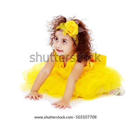 Funny curly little girl in a bright yellow elegant dress crawling on the floor. She looks to the top.Isolated on white background.