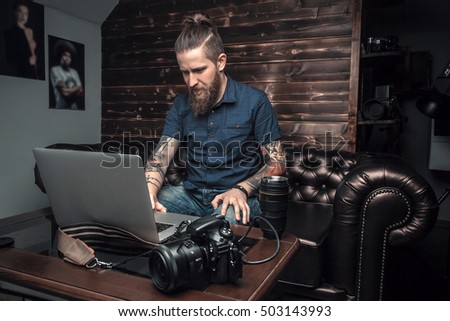 Beautiful portrait of the photographer at the workplace. The concept of the creative process, skill and favorite pastime. Male boss sitting on the couch in his office, working on laptop