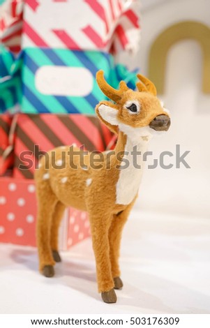 Realistic White-tailed Deer Fawn (Odocoileus virginianus) Animal Replica Prop Fur Toy, for Decoration, Selective Focus, with abstract colorful boxes of present on the background. Christmas concept.