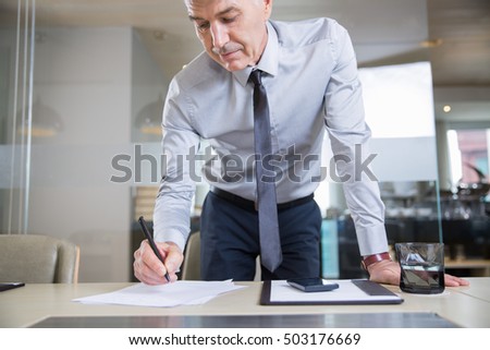 Senior Businessman Bending over Desk and Writing