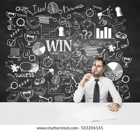 Thoughtful and confused young businessman at workplace with creative business sketch on chalkboard background. Success concept