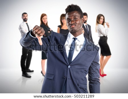 Handsome black man doing bad signal with many people behind