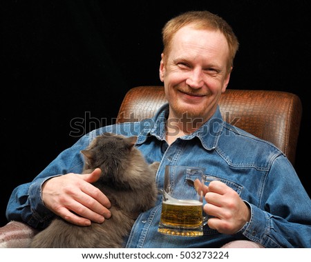 Happy man with a mug of beer and cat in the chair. black Background
