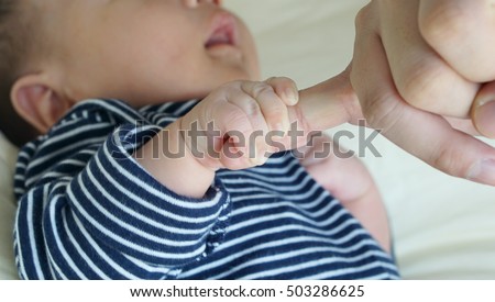Baby's hand, with long sleeve striped suit, holding adult little finger