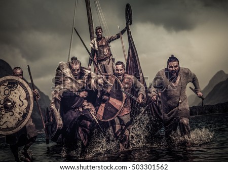 Mad vikings warriors in the attack, running along the shore with Drakkar on the background. Royalty-Free Stock Photo #503301562