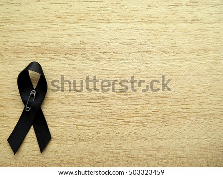 Condolences black ribbon on the pin with the wooden background. To show the sorrow with the grief on the passing of people. These ribbons can be pinned on shirts or clothes.