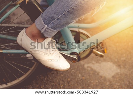 Female wearing jeans and wearing white shoes rides bicycle on the park