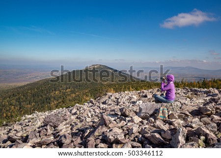 Girl tourist sitting on stones with a photo camera in mountains at forest background Tourism with light baggage