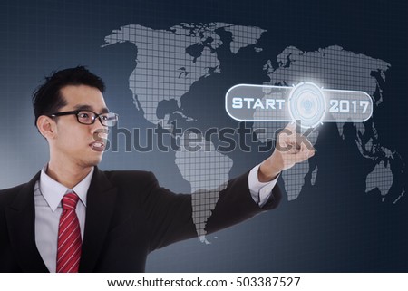 Picture of Asian businessman touching start button with numbers 2017 and world map on the virtual screen