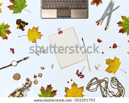 Autumn composition with laptop, dry flowers, autumn leaves, colour pencils, brush, and tablet with a blank sheet of paper. Top view on light blue background. Mock up for art work with workplace.