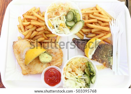 fish and chips with coleslaw, lemon and herb butter on paper plate takeout