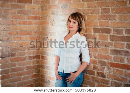 pretty girl in a white shirt and blue jeans against a brick wall 
