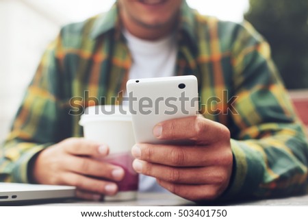 Young man with cup of coffee and smartphone listing news feed, sitting in street cafe Royalty-Free Stock Photo #503401750
