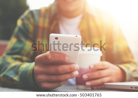Young man with cup of coffee and smartphone in hand sitting in street cafe, listing news feed Royalty-Free Stock Photo #503401765